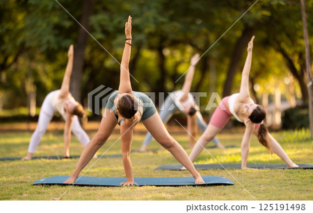 Athletic girls meditates in yoga pose parshvottanasana in summer sunny park. Demonstration of various yoga poses Athletic girls meditates in yoga pose parshvottanasana in summer sunny park. Demonstration of various yoga poses 125191498