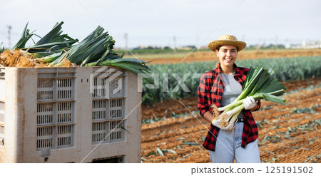 Happy girl farmer posing on plantation holding harvested leeks Happy girl farmer posing on plantation holding harvested leeks 125191502