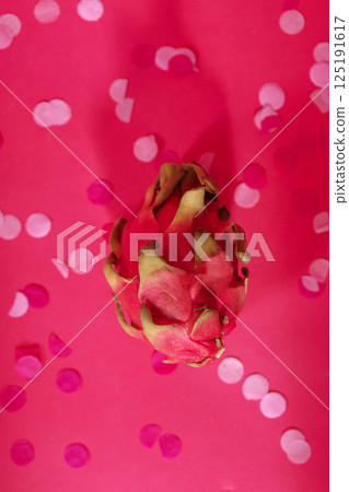 Close-up of a fresh dragon fruit on a pink background with confetti. Cactus fruit on a bright backdrop. Close-up of a fresh dragon fruit on a pink background with confetti. Cactus fruit on a bright backdrop. 125191617