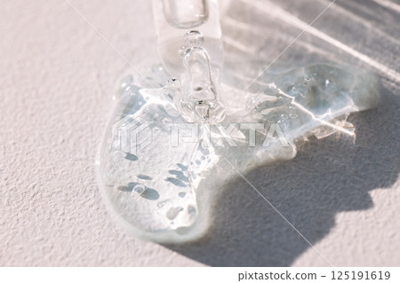 Close-up of a glass pipette with transparent gel with bubbles. Cosmetic products. A dropper of moisturizing serum or vitamin essence on a textured background. Close-up of a glass pipette with transparent gel with bubbles. Cosmetic products. A dropper of moisturizing serum or vitamin essence on a textured background. 125191619
