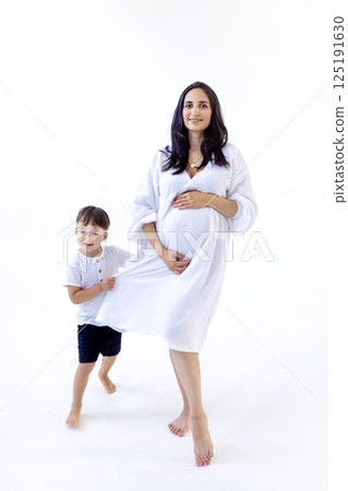 A young pregnant woman in a white dress with her cute son. A little boy gently hugs the belly A young pregnant woman in a white dress with her cute son. A little boy gently hugs the belly 125191630