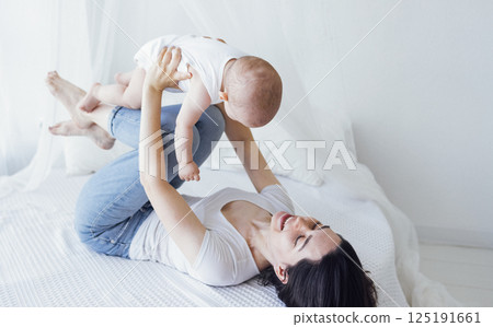 Pretty infant in a white bodysuit with his mom on a light background. Motherhood concept. 125191661