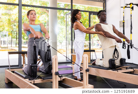 Woman performing set of pilates exercises on reformer in modern fitness studio Woman performing set of pilates exercises on reformer in modern fitness studio 125191689