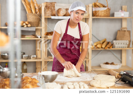 Young woman works in bakery as baker, kneads and prepare dough, works with flour. 125191690