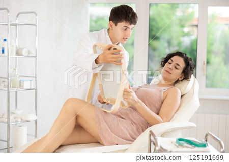 Middle-aged woman having consultation about face aesthetic while looking in the mirror Middle-aged woman having consultation about face aesthetic while looking in the mirror 125191699