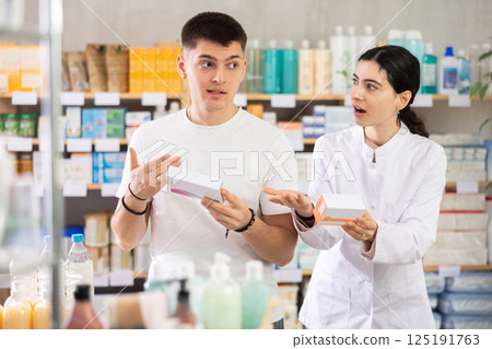 Guy chooses pills in modern pharmacy. Female pharmacist helps with choosing medicine 125191763