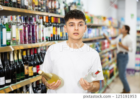 Young male customer deciding on buying bottle of wine or vodka 125191953