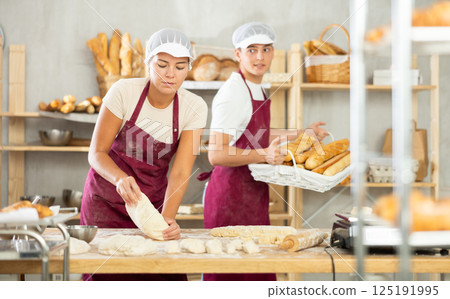 Young female baker kneading dough on flour-dusted table in artisan bakery Young female baker kneading dough on flour-dusted table in artisan bakery 125191995