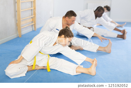 Woman and men in kimonos doing stretching before karate training Woman and men in kimonos doing stretching before karate training 125192052