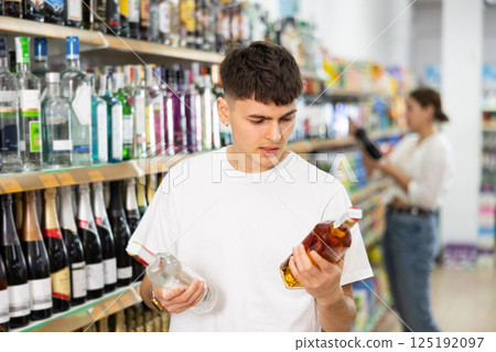 Thoughtful young guy choosing alcoholic drinks in supermarket 125192097