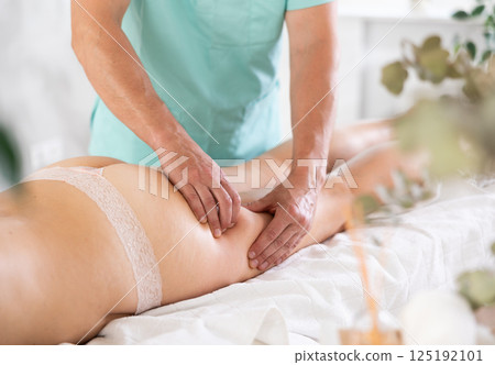 Woman covered with white towel lies and enjoys during anti-cellulite massage in hips and legs Woman covered with white towel lies and enjoys during anti-cellulite massage in hips and legs 125192101