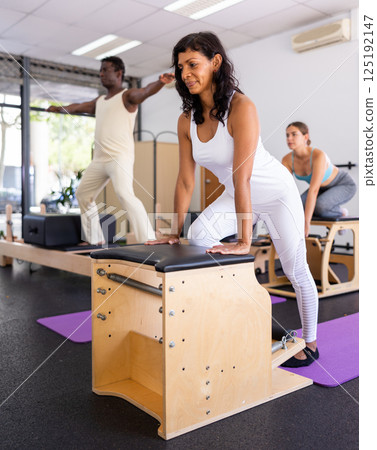 Hispanic woman doing exercises on pilates chair during group training 125192147