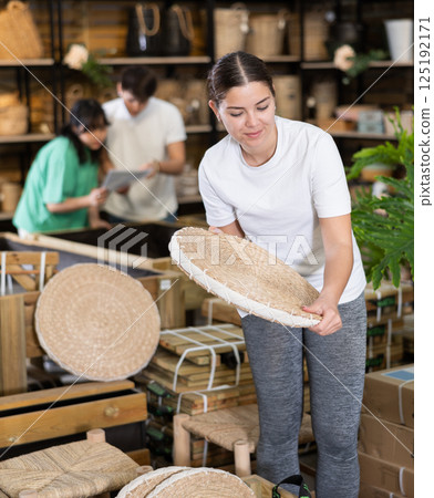 woman examines round pillow made of wicker for garden furniture before buying woman examines round pillow made of wicker for garden furniture before buying 125192171
