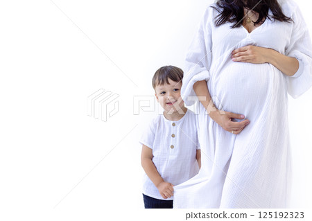 A young pregnant woman in a white dress with her cute son. A little boy gently hugs the belly A young pregnant woman in a white dress with her cute son. A little boy gently hugs the belly 125192323