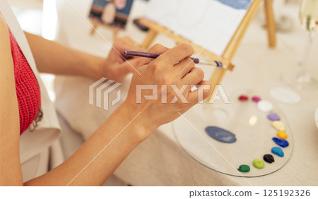Close-up of woman hands and a palette with paints. The artist holds a brush and mixes acrylic paints 125192326