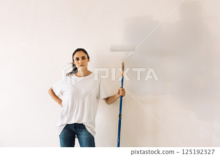 A laughing young woman in T-shirt paints a wall white in a house. A laughing young woman in T-shirt paints a wall white in a house. 125192327