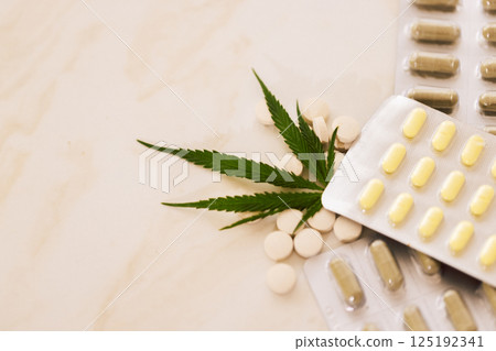 Mockups of medicines on a beige background with cannabis leaf. Close up of blisters with pills on a marble table with green hemp. 125192341