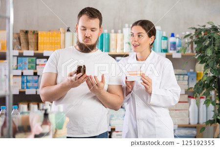 Man chooses cough syrup in modern pharmacy. Female pharmacist helps with choosing medicine 125192355