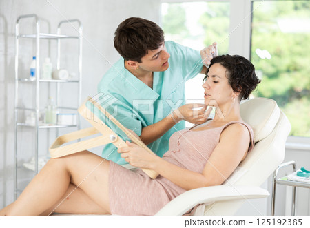 Middle-aged woman having consultation about face aesthetic while looking in the mirror 125192385