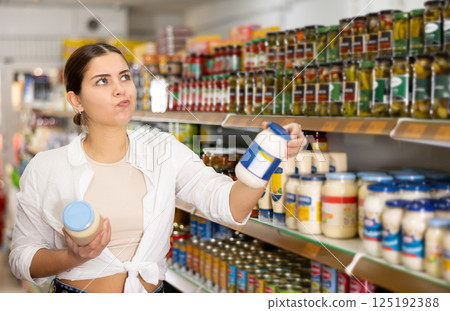 Young female customer diligently picking out jar of mayonnaise 125192388