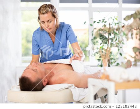 woman covers the man with a towel before massage procedures 125192448