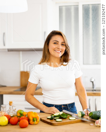 Smiling young Hispanic woman preparing salad in home kitchen Smiling young Hispanic woman preparing salad in home kitchen 125192477