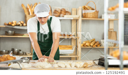 Young male baker kneads the dough in bakery 125192491