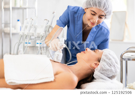 Young female cosmetologist performs whitening procedure on collarbones of young woman 125192506