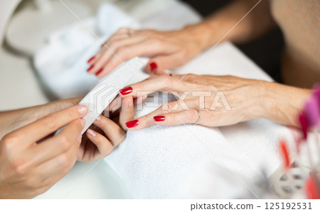 Hands of young girl manicurist perform trimming saws nails to elderly lady client. 125192531