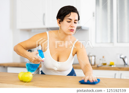 Woman cleaning kitchen countertop with cleaning spray and rag Woman cleaning kitchen countertop with cleaning spray and rag 125192539