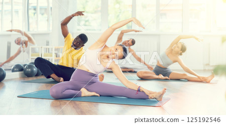 Asian woman performing seated Mermaid stretch in group Pilates class Asian woman performing seated Mermaid stretch in group Pilates class 125192546