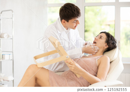 Male beautician giving consultation to woman patient with mirror in aesthetic clinic 125192555