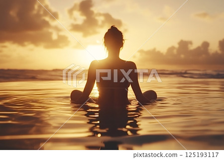 Woman meditating in lotus pose at golden sunset on beach 125193117