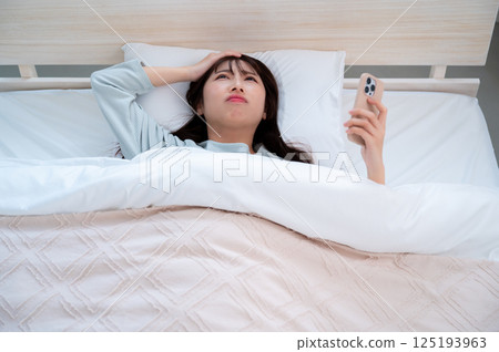 A young woman holding her head looking at her smartphone 125193963