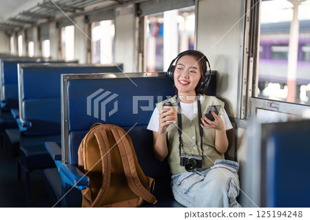 Savoring the Moment and Travel. A joyful traveler enjoys her drink while listening to music on the train. 125194248