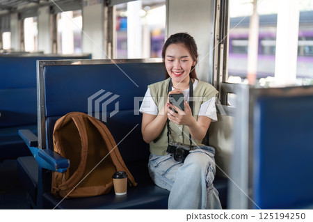 Joy and Exploration. A woman smiles as she interacts with her smartphone on a train journey. Joy and Exploration. A woman smiles as she interacts with her smartphone on a train journey. 125194250