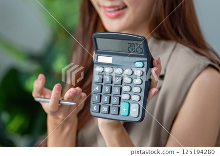 Calculator Insights and Financial Planning. A woman revealing her calculator displaying a financial figure. 125194280