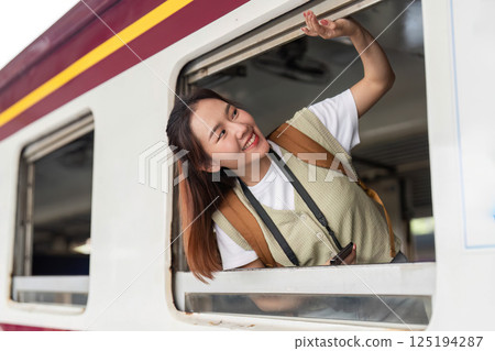 Travel Enthusiasm and Scenic Views. A young woman leaning out the train window, enjoying the fresh air and scenery. 125194287