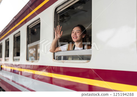 Goodbyes and Travel Memories. A young woman waves while enjoying a train journey, capturing a moment of joy. 125194288