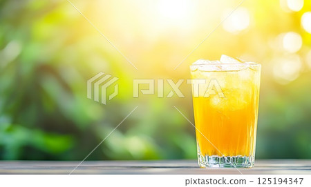 Refreshing glass of iced orange juice in sunlit garden setting. 125194347
