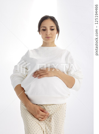 A stylish pregnant woman gently holds onto her belly. The expectant mother touches her tummy A stylish pregnant woman gently holds onto her belly. The expectant mother touches her tummy 125194466