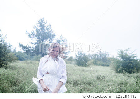 A close-up portrait of a laughing young woman in a white dress in the rain 125194482