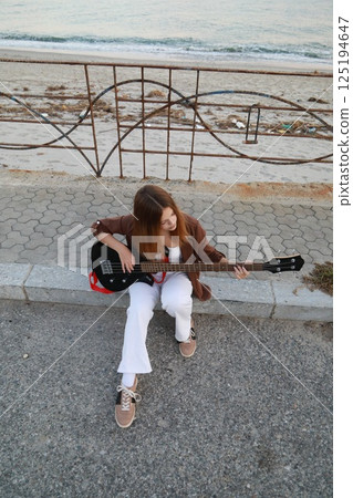 Girl Plays The Bass Instrument Sitting On The Step Near The Street At Evening 125194647