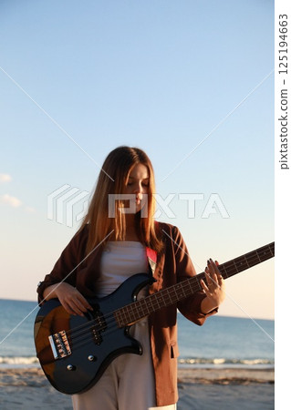 Girl Plays Bass Music Instrument On The Beach At Sunset Near Ocean 125194663