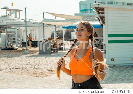 Woman Beach Summer: Young woman adjusts pigtails, sunny beach day, casual summer attire. Woman Beach Summer: Young woman adjusts pigtails, sunny beach day, casual summer attire. 125195306