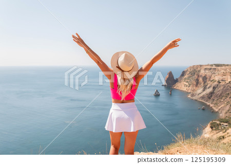 A woman in a pink top and white skirt stands on a hill overlooking the ocean A woman in a pink top and white skirt stands on a hill overlooking the ocean 125195309