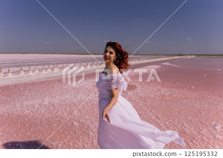 Woman White Dress Pink Salt Lake - A woman in a white dress walks on a pink salt lake, the wind blowing her hair and dress. Woman White Dress Pink Salt Lake - A woman in a white dress walks on a pink salt lake, the wind blowing her hair and dress. 125195332