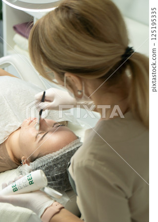 Eyebrow Tinting Salon Treatment: Beautician applying dye to client's eyebrows. 125195335