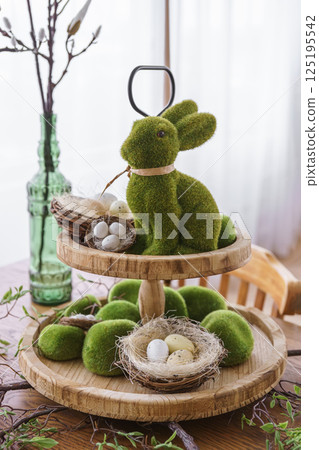 Green moss Easter Bunny and decorative Easter eggs in nest on on two tiered wooden plate Green moss Easter Bunny and decorative Easter eggs in nest on on two tiered wooden plate 125195542