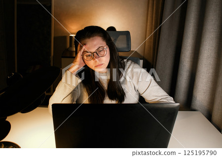Hard working woman works on computer in her home office and tries to solve work problems. Feeling despair and burnt out from job issues. Hard working woman works on computer in her home office and tries to solve work problems. Feeling despair and burnt out from job issues. 125195790